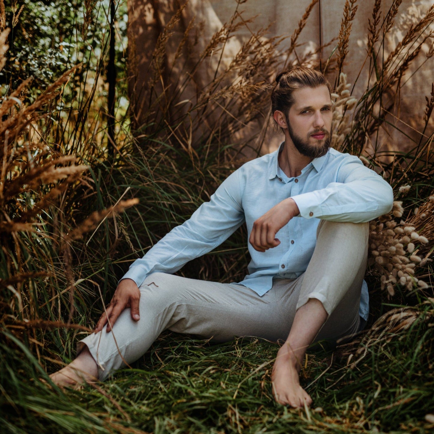 Man sitting in a field of tall grass and wildflowers with a blurred natural background

