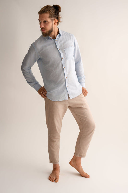 Man wearing a light blue shirt and beige pants on a plain background